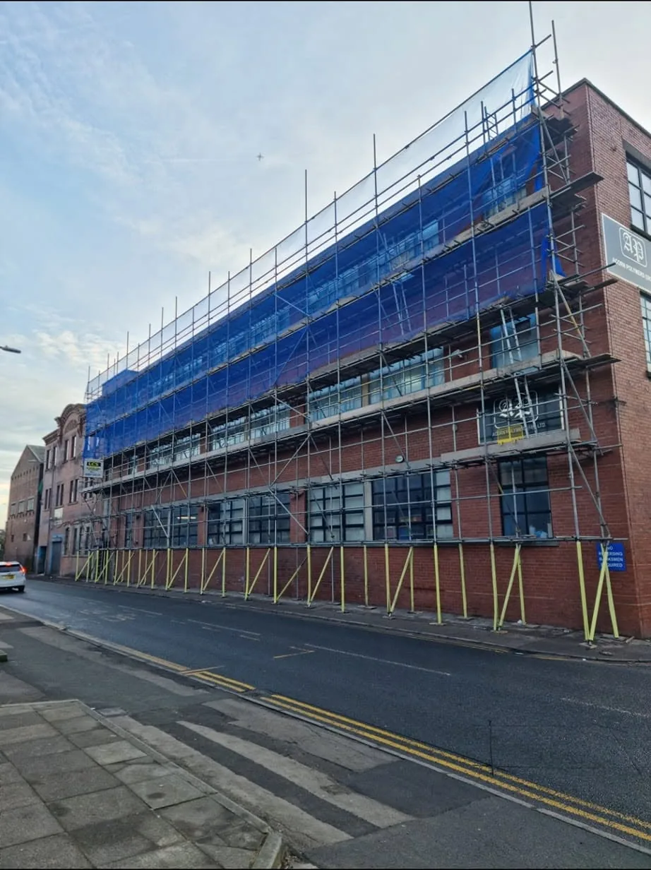 Commercial scaffold with blue debris netting along a road frontage